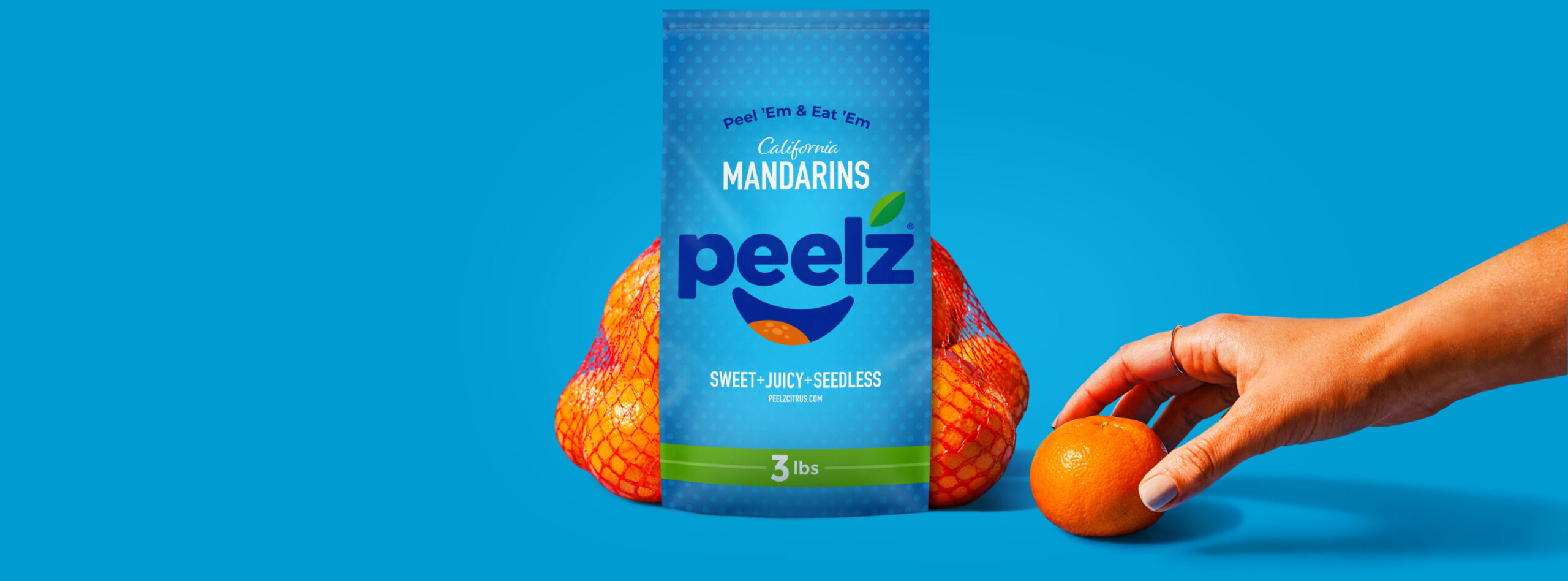 Peelz mandarins packed with a hand reaching for a mandarin sitting in front of the bag