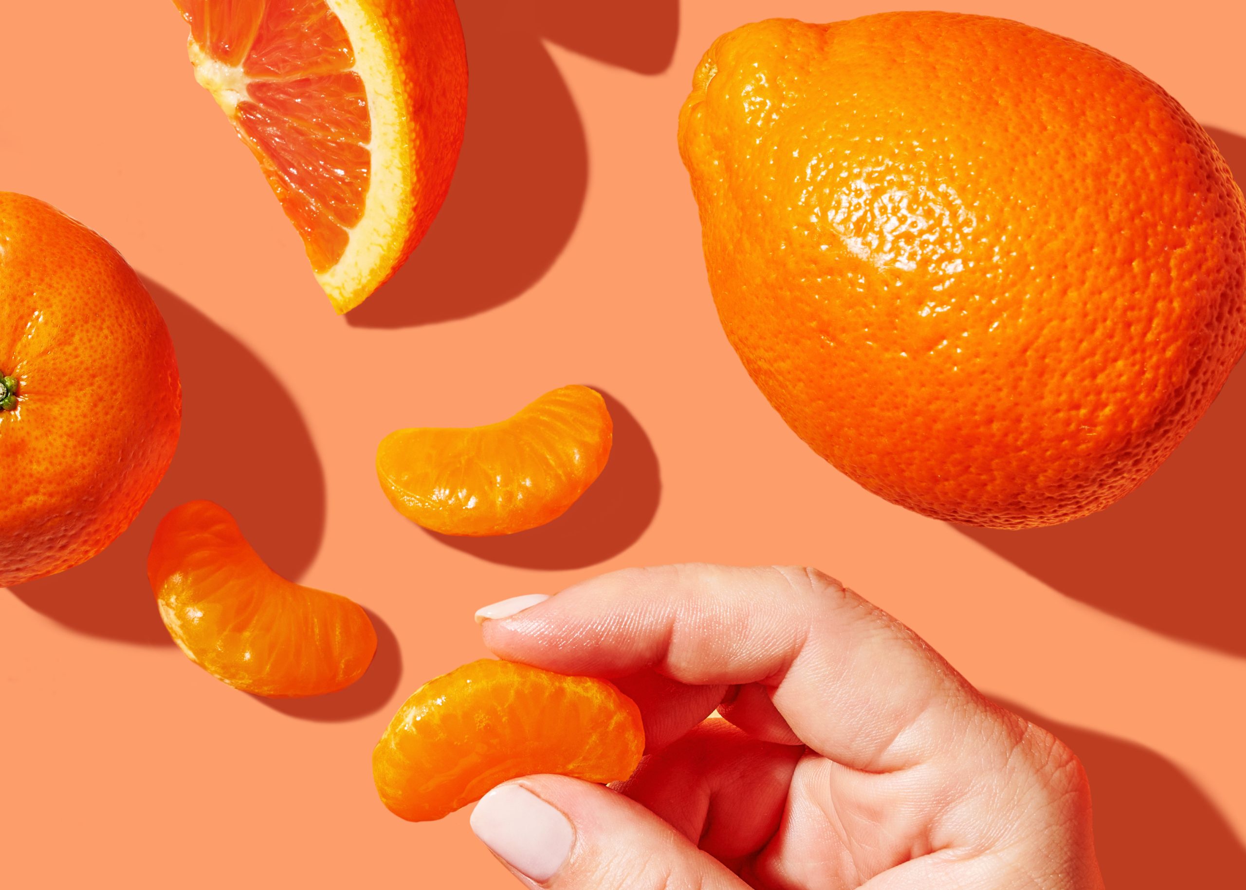 A photoshoot-style shot of citrus including grapefruit and clementines with a hand holding a slice