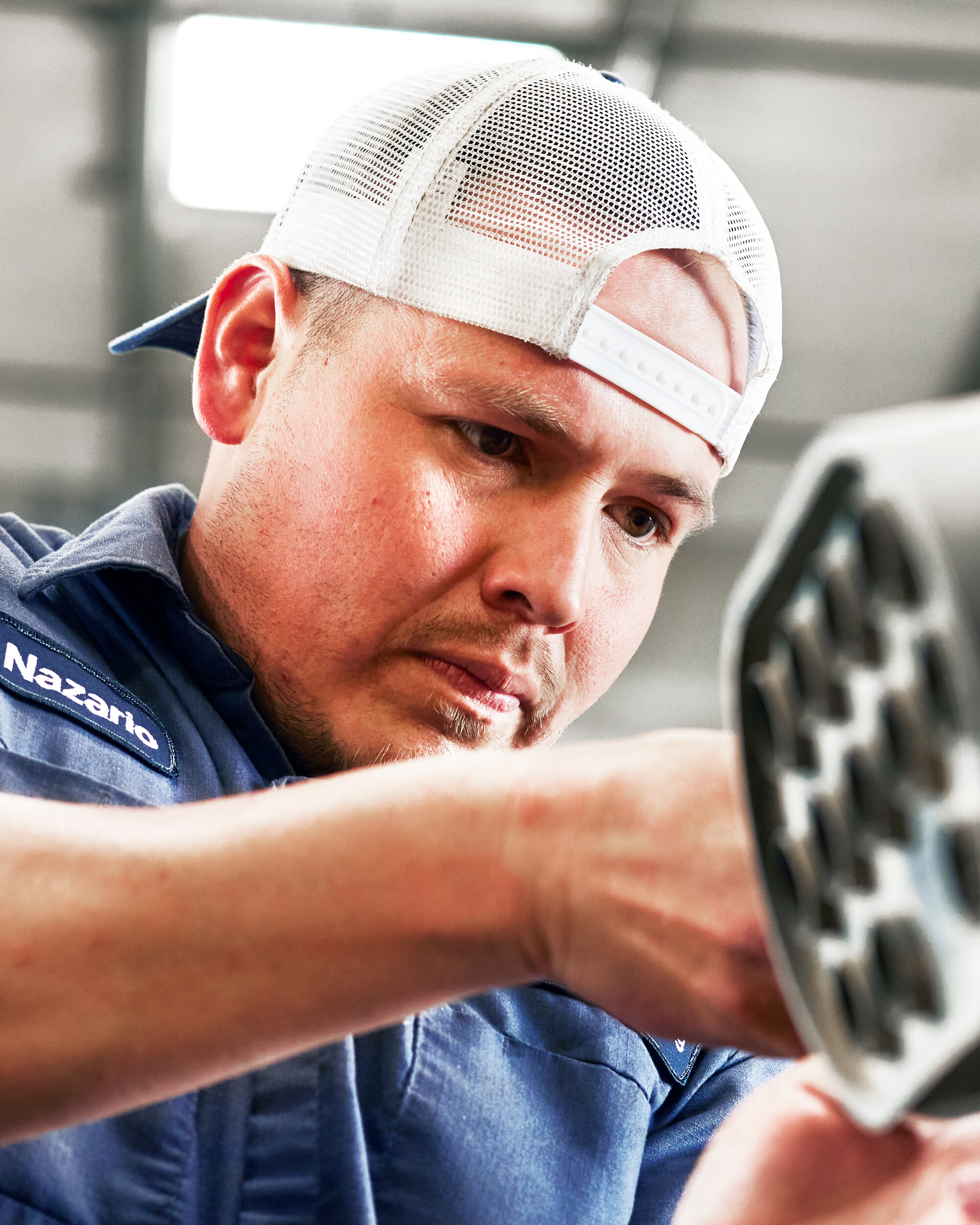 Man wearing a white cap backwards and a navy polo is working on a machine in a company
