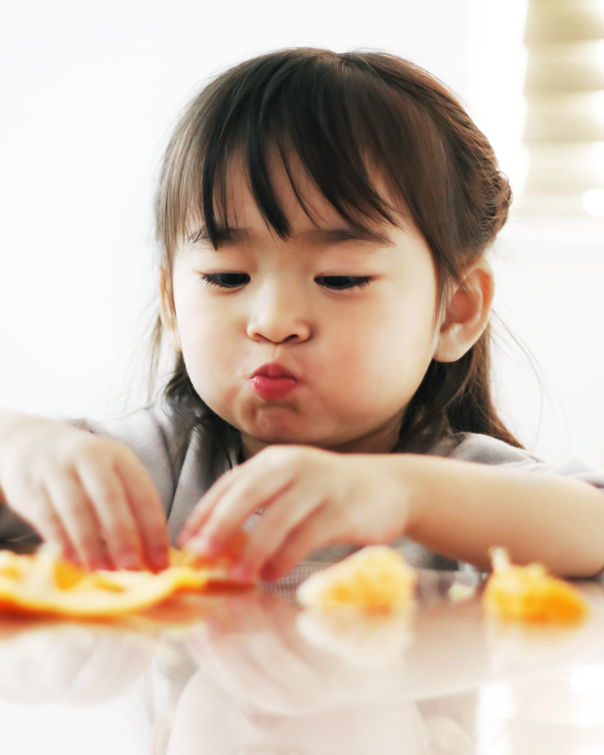 Young girl is sitting at a table, peeling and eating a clementine