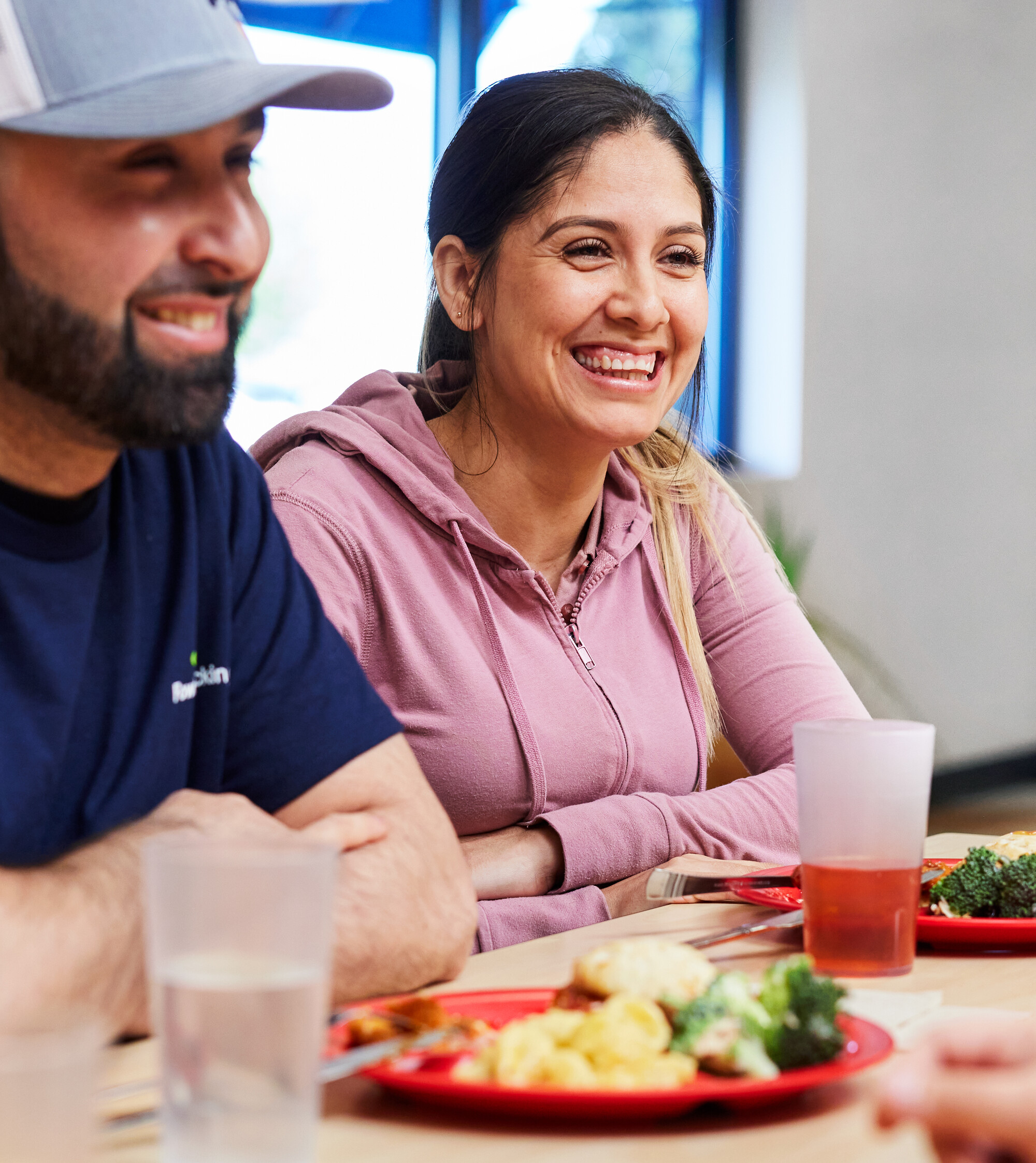 Two people are sitting with their arms crossed in an office smiling and looking at something