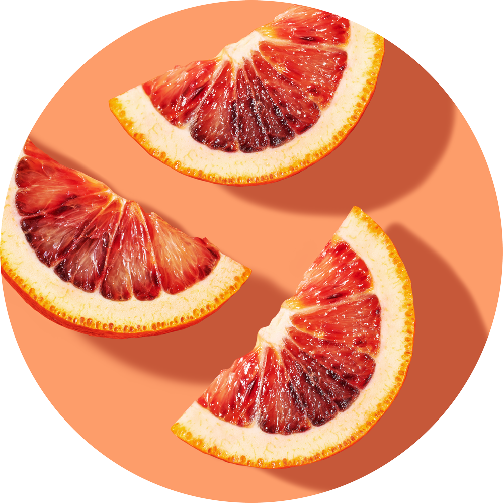 Three slices of a red grapefruit are sitting on top of a coral colored backdrop